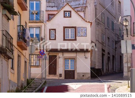 Small traditional house with a steep roof and azulejo tile panel on a narrow street in the Alfama district of Lisbon, Portugal. Small traditional house with a steep roof and azulejo tile panel on a narrow street in the Alfama district of Lisbon, Portugal. 141089515