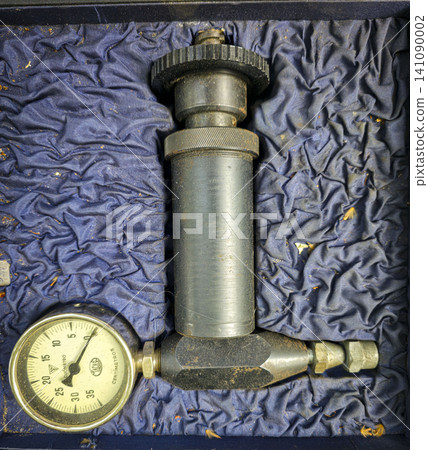 A manual pump tool with a pressure gauge sits inside a blue lined storage case. The tool shows wear from use and is ready for various tasks and projects. A manual pump tool with a pressure gauge sits inside a blue lined storage case. The tool shows wear from use and is ready for various tasks and projects. 141090002