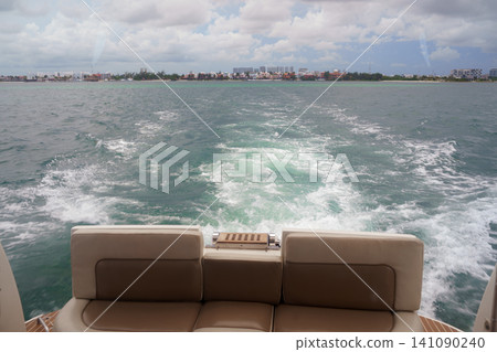 Boat wake trailing toward distant coastal city skyline Boat wake trailing toward distant coastal city skyline 141090240