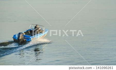 A blue speedboat races across calm blue water in bright daylight. A blue speedboat races across calm blue water in bright daylight. 141090261