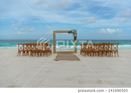 Beach wedding setup with wooden frame arch and rows of chairs by ocean Beach wedding setup with wooden frame arch and rows of chairs by ocean 141090305