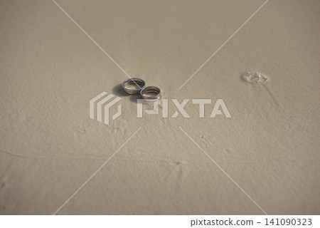 Wedding rings lying together on wet sandy beach Wedding rings lying together on wet sandy beach 141090323