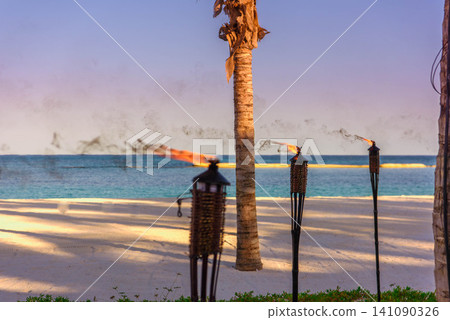 Tiki torches burning on tropical beach at dusk Tiki torches burning on tropical beach at dusk 141090326