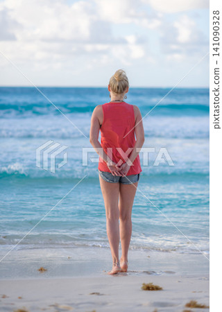Blonde woman standing barefoot on tropical beach shore Blonde woman standing barefoot on tropical beach shore 141090328