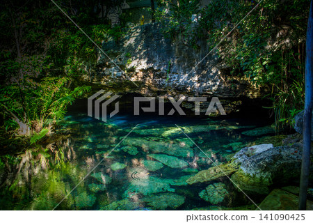 Sunlit cenote pool surrounded by jungle rocks Sunlit cenote pool surrounded by jungle rocks 141090425