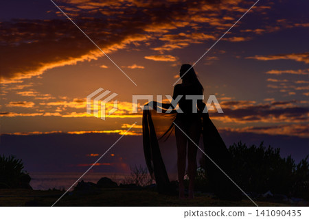 Woman silhouette with flowing fabric against dramatic sunset sky Woman silhouette with flowing fabric against dramatic sunset sky 141090435