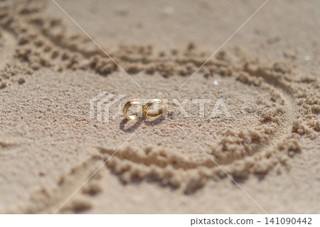 Golden wedding rings inside heart drawn on tropical sand 141090442