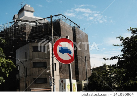 A sign prohibiting large trucks and other heavy vehicles stands against a backdrop of a building under construction and a blue sky. A sign prohibiting large trucks and other heavy vehicles stands against a backdrop of a building under construction and a blue sky. 141090904