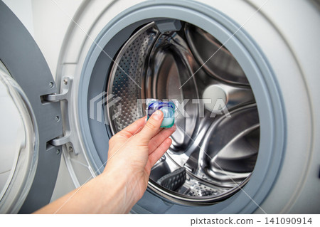 Person adds detergent pod into washing machine for effective laundry cleaning Person adds detergent pod into washing machine for effective laundry cleaning 141090914