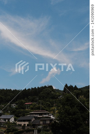 Houses built on the lush green slopes of a mountain, under a blue sky and white clouds. Houses built on the lush green slopes of a mountain, under a blue sky and white clouds. 141090969
