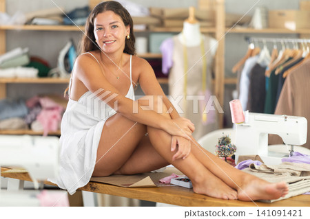 Relaxed young dressmaker taking break barefoot on sewing table Relaxed young dressmaker taking break barefoot on sewing table 141091421