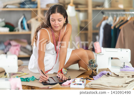 Female clothing designer creating sketches on tablet in atelier Female clothing designer creating sketches on tablet in atelier 141091490