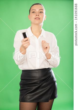 Chroma key compositing. Pretty girl with a remote control is giving presentation Chroma key compositing. Pretty girl with a remote control is giving presentation 141091688