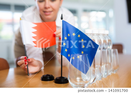 Young woman puts Qatar and EU flags on table in office 141091700