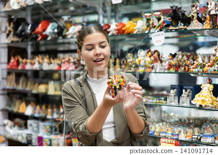 Cheerful female tourist choosing colorful bull statuette at tourist shop Cheerful female tourist choosing colorful bull statuette at tourist shop 141091714