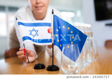 Employee of delegation prepares negotiating table - sets up flag of European Union and Israel Employee of delegation prepares negotiating table - sets up flag of European Union and Israel 141091717