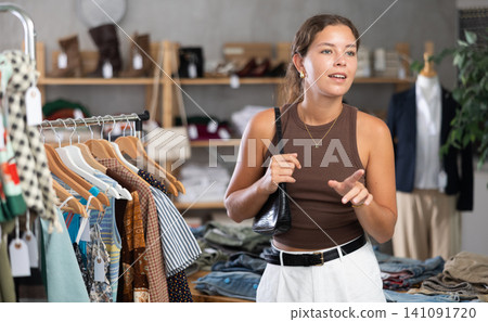 Young woman comes to boutique and looks at clothes Young woman comes to boutique and looks at clothes 141091720