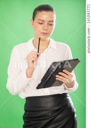 Chroma key compositing. Pretty girl takes notes in electronic tablet on green background Chroma key compositing. Pretty girl takes notes in electronic tablet on green background 141091771