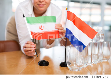 Businesswoman arranging the flags of Iran and Netherlands for presentation and negotiations Businesswoman arranging the flags of Iran and Netherlands for presentation and negotiations 141091787