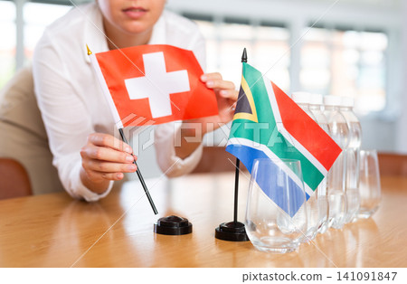 Little flag of South Africa on table and flag of Switzerland put next to it by young woman Little flag of South Africa on table and flag of Switzerland put next to it by young woman 141091847