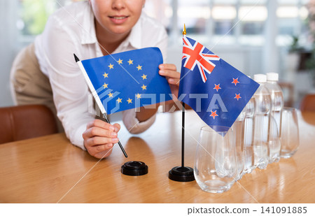 Woman secretary prepares an office for negotiations - she places flags of Australia and European Union table Woman secretary prepares an office for negotiations - she places flags of Australia and European Union table 141091885