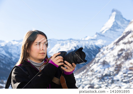 Traveler woman taking pictures of winter Swiss Alps with camera Traveler woman taking pictures of winter Swiss Alps with camera 141091895