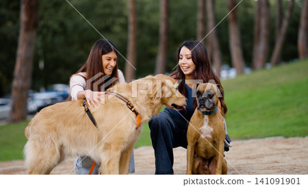 Two women enjoying park with golden retriever and boxer dog Two women enjoying park with golden retriever and boxer dog 141091901