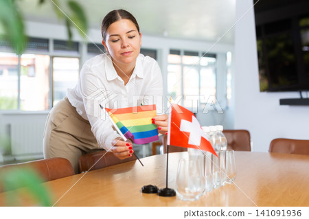 Positive young woman putting little LGBT flag on table next to the flag of Switzerland Positive young woman putting little LGBT flag on table next to the flag of Switzerland 141091936
