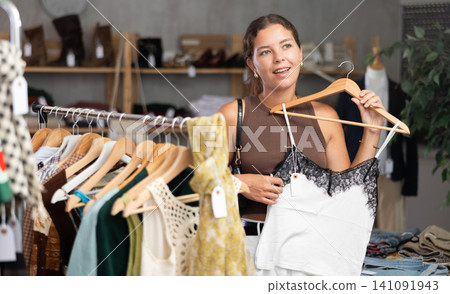 Girl customer choose crop top in store, and buyer carefully examines product. Girl customer choose crop top in store, and buyer carefully examines product. 141091943