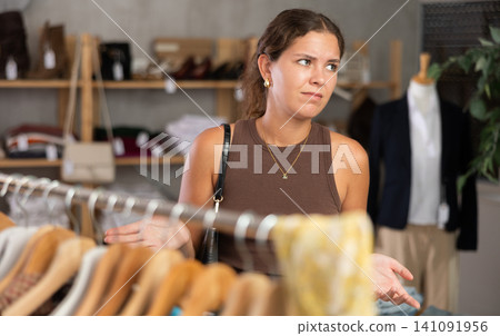 Young woman looking upset at clothes in store Young woman looking upset at clothes in store 141091956