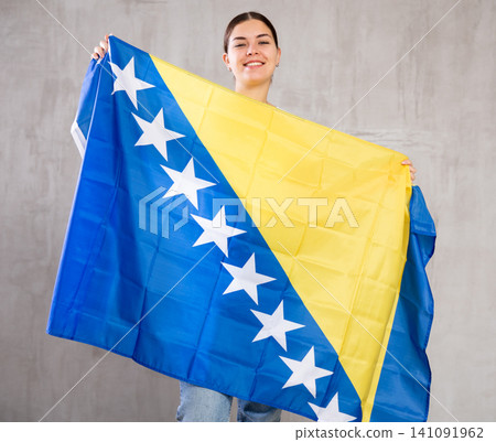 Happy girl stands with Bosnian flag.Isolated on gray background Happy girl stands with Bosnian flag.Isolated on gray background 141091962