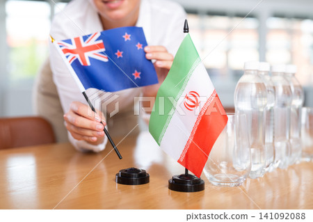 Woman secretary prepares an office for negotiations - she places flags of Iran and Australia table Woman secretary prepares an office for negotiations - she places flags of Iran and Australia table 141092088