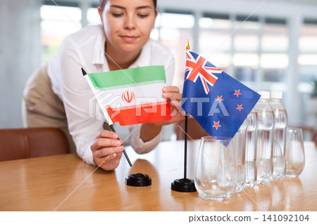 Woman secretary prepares an office for negotiations - she places flags of Iran and Australia table Woman secretary prepares an office for negotiations - she places flags of Iran and Australia table 141092104