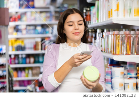 Female shopper scanning a QR code using a mobile phone in cosmetics store Female shopper scanning a QR code using a mobile phone in cosmetics store 141092128