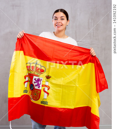 Joyful smiling young woman waving state flag of Spain against gray wall background Joyful smiling young woman waving state flag of Spain against gray wall background 141092192
