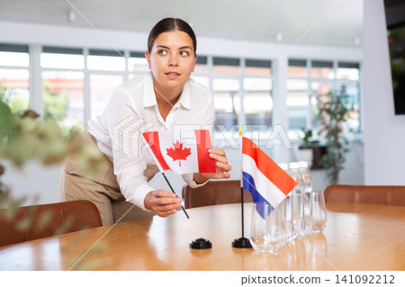 Young woman putting Canada and Netherlands flags on table in office Young woman putting Canada and Netherlands flags on table in office 141092212