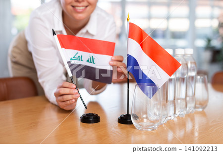 Businesswoman arranging the flags of Iraq and Netherlands for presentation and negotiations Businesswoman arranging the flags of Iraq and Netherlands for presentation and negotiations 141092213