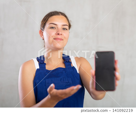 Young woman in work overalls posing with phone Young woman in work overalls posing with phone 141092219