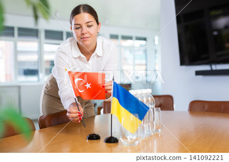Young woman setting flags of Ukraine and Turkey on negotiating table Young woman setting flags of Ukraine and Turkey on negotiating table 141092221