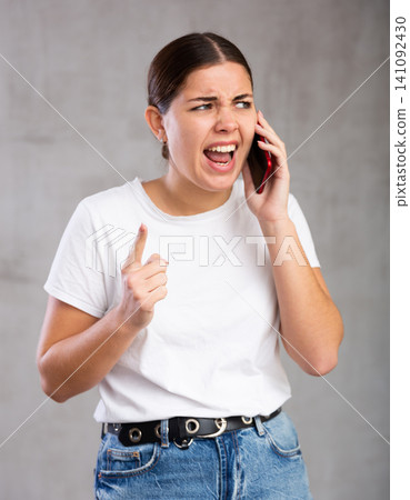 Indignant young woman talking on mobile phone Indignant young woman talking on mobile phone 141092430