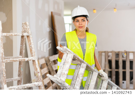 Young woman builder carrying stepladder Young woman builder carrying stepladder 141092743