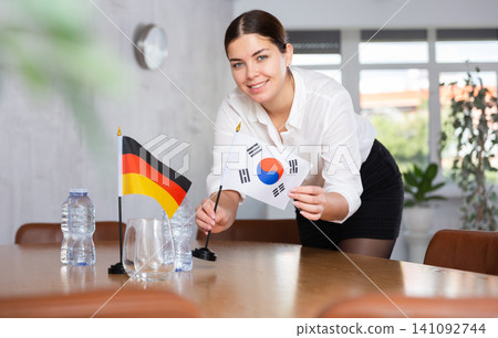Young female attendant putting up flags for international negotiations between germany and south korea Young female attendant putting up flags for international negotiations between germany and south korea 141092744