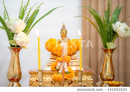 Golden Buddha statue with lotus flowers, marigold garlands, and lit candles on a peaceful Thai Buddhist Golden Buddha statue with lotus flowers, marigold garlands, and lit candles on a peaceful Thai Buddhist 141092820