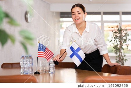 Young female attendant putting up flags for international negotiations between usa and finland Young female attendant putting up flags for international negotiations between usa and finland 141092866