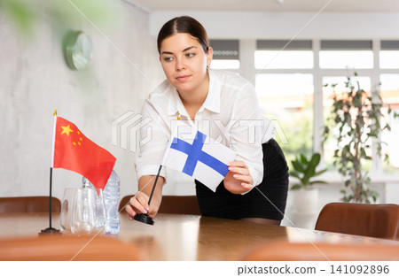 Preparing for business negotiations - woman sets small flags of countries of China and Finland on table Preparing for business negotiations - woman sets small flags of countries of China and Finland on table 141092896