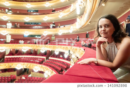 Girl visiting opera theater from upper floor of dress circle looks at stage and watches performance Girl visiting opera theater from upper floor of dress circle looks at stage and watches performance 141092898