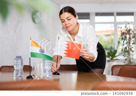Young female attendant putting up flags for international negotiations between india and bahrain 141092938
