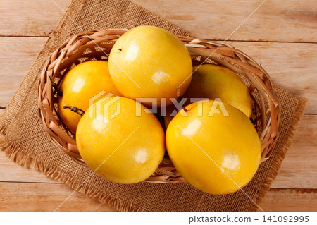 Wicker basket with fresh yellow passion fruit on jute fabric and a light wood surface. Wicker basket with fresh yellow passion fruit on jute fabric and a light wood surface. 141092995