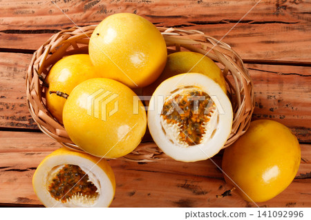Whole and cut yellow passion fruits revealing fresh pulp and seeds on a wicker basket on a rustic wooden table 141092996