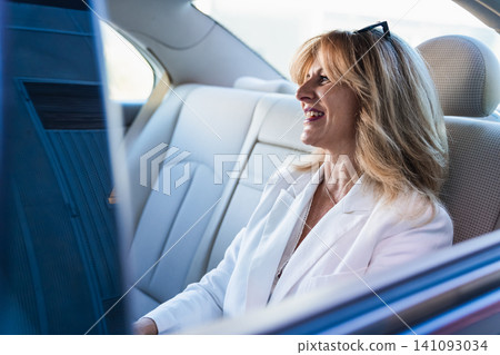 Businesswoman smiling in luxury car back seat Businesswoman smiling in luxury car back seat 141093034